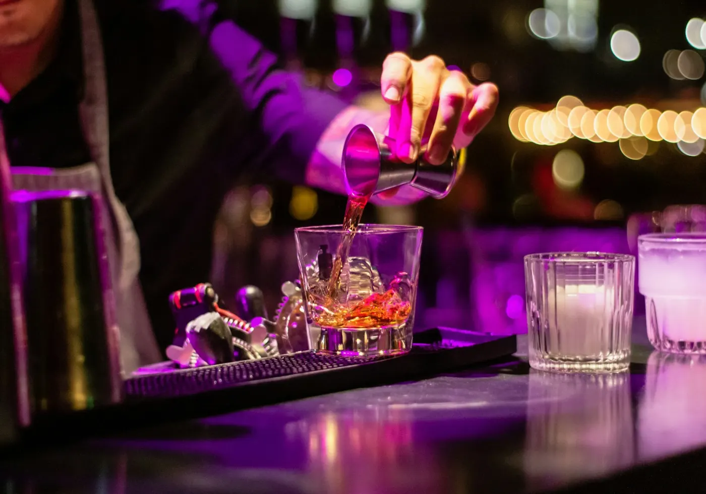 A bartender pouring a drink along a busy, softly lit bar
