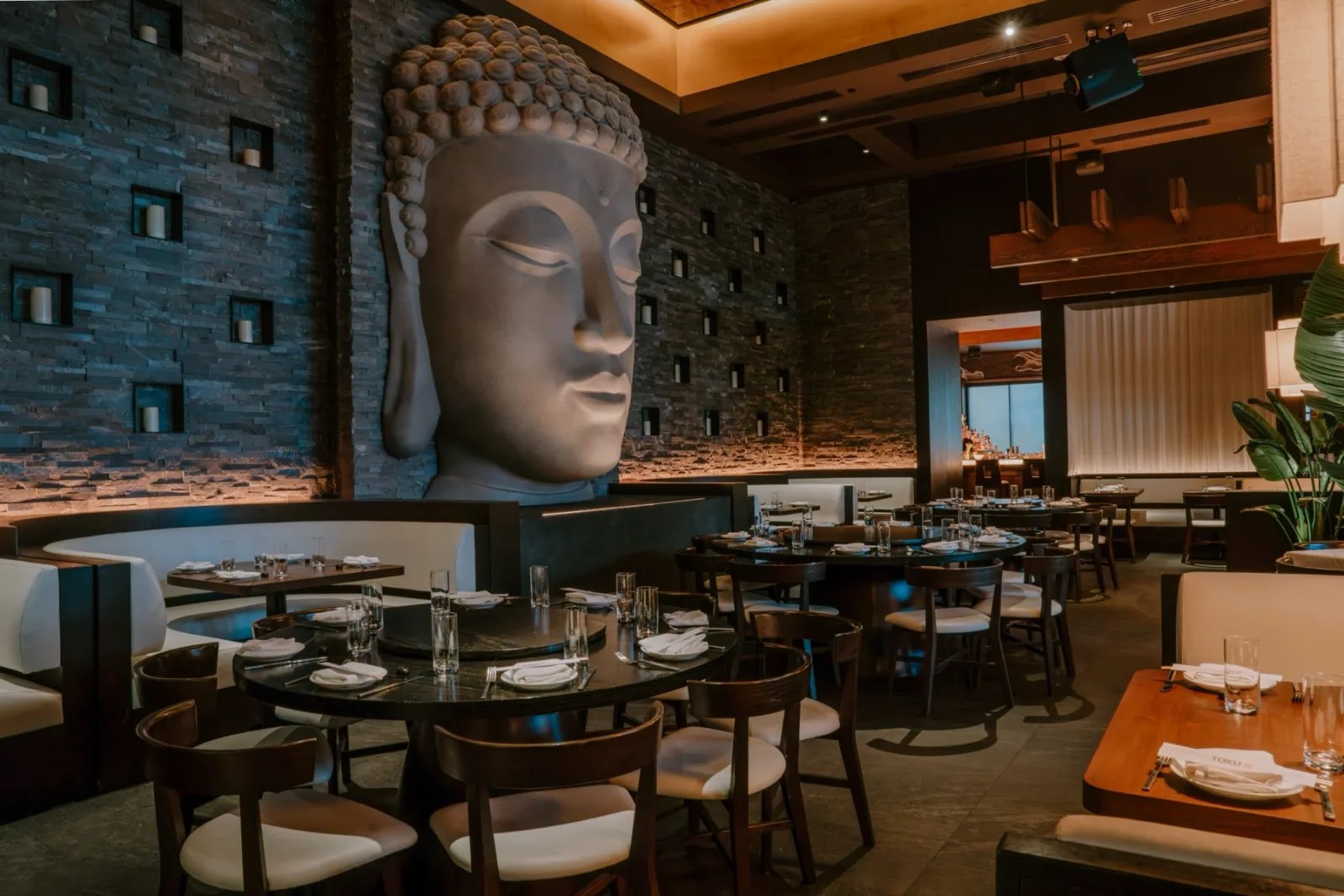 A large restaurant dining room with set tables, stone walls and a speaker mounted discreetly in the ceiling
