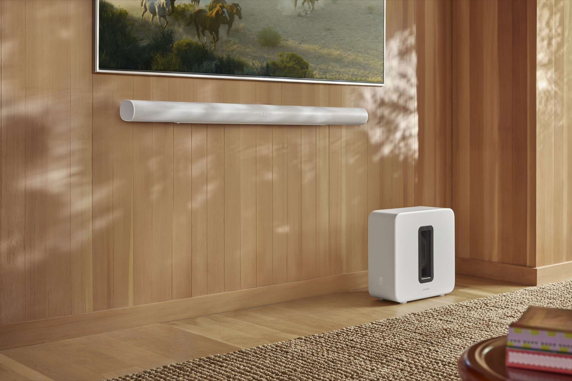 White Sonos Arc Ultra wall mounted beneath a TV with a white Sub 4 nearby